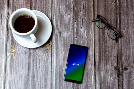 02/10/2021 Portsmouth, Hampshire, UK A mobile phone or cell phone laid on a wooden table with the SSE energy app open on screen next to a coffeeのeditorial素材