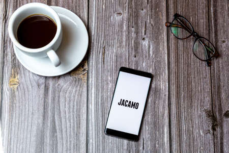 02/10/2021 Portsmouth, Hampshire, UK A mobile phone or cell phone laid on a wooden table with the jacamo mens fashion app open on screen next to a coffeeのeditorial素材