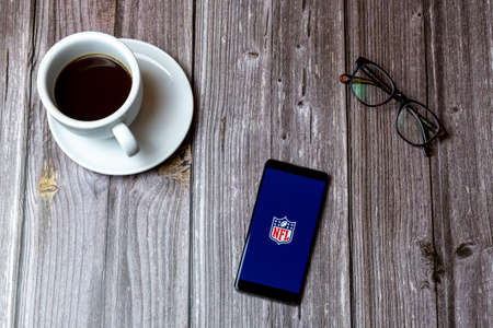 02/10/2021 Portsmouth, Hampshire, UK A mobile phone or cell phone laid on a wooden table with the NFL app open on screen next to a coffeeのeditorial素材