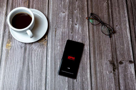 02/10/2021 Portsmouth, Hampshire, UK A mobile phone or cell phone laid on a wooden table with the AMC cinemas app open on screen next to a coffeeのeditorial素材
