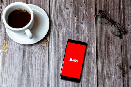 02/10/2021 Portsmouth, Hampshire, UK A mobile phone or cell phone laid on a wooden table with the Sun Newspaper app open on screen next to a coffeeのeditorial素材