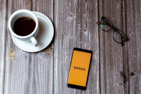 02/10/2021 Portsmouth, Hampshire, UK A mobile phone or cell phone laid on a wooden table with the Sonos app open on screen next to a coffeeのeditorial素材