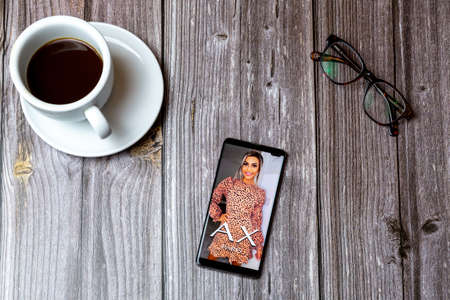 02/10/2021 Portsmouth, Hampshire, UK A mobile phone or cell phone laid on a wooden table with the AX Paris fashion app open on screen next to a coffeeのeditorial素材