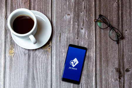 02/10/2021 Portsmouth, Hampshire, UK A mobile phone or cell phone laid on a wooden table with the CV Library job search app open on screenのeditorial素材