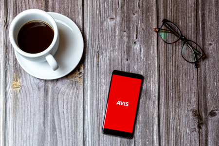 02/10/2021 Portsmouth, Hampshire, UK A mobile phone or cell phone laid on a wooden table with the AVIS app open on screen next to a coffeeのeditorial素材