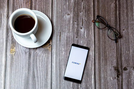 02/10/2021 Portsmouth, Hampshire, UK A mobile phone or cell phone laid on a wooden table with the Coral Betting app open on screen next to a coffeeのeditorial素材