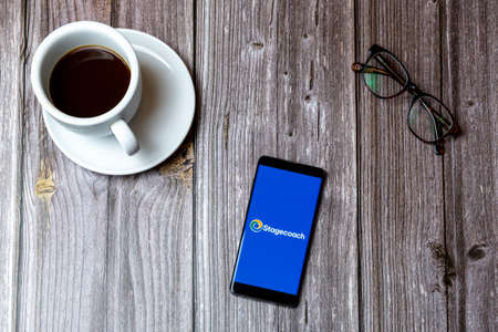 02/10/2021 Portsmouth, Hampshire, UK A mobile phone or cell phone laid on a wooden table with the stagecoach bus app open on screen next to a coffeeのeditorial素材