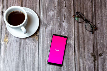 02/10/2021 Portsmouth, Hampshire, UK A mobile phone or cell phone laid on a wooden table with the radish app open on screen next to a coffeeのeditorial素材
