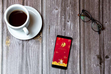 02/10/2021 Portsmouth, Hampshire, UK A mobile phone or cell phone laid on a wooden table with the Fly Malaysia app open on screen next to a coffeeのeditorial素材