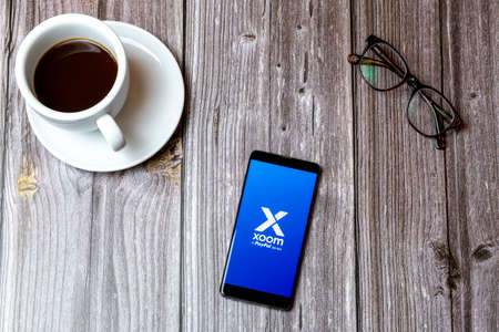 02/10/2021 Portsmouth, Hampshire, UK A mobile phone or cell phone laid on a wooden table with the Xoom paypal app open on screen next to a coffeeのeditorial素材