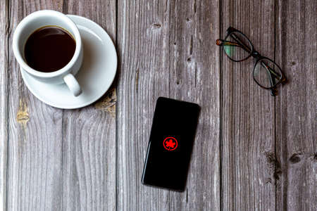 02/10/2021 Portsmouth, Hampshire, UK A mobile phone or cell phone laid on a wooden table with the Canada airlines app open on screen next to a coffeeのeditorial素材