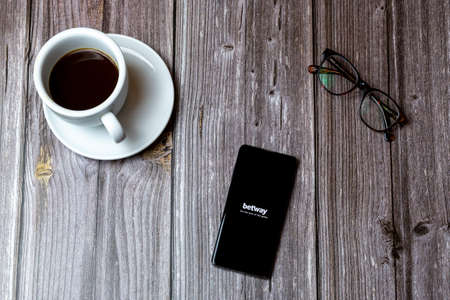 02/10/2021 Portsmouth, Hampshire, UK A mobile phone or cell phone laid on a wooden table with the Betway betting app open on screen next to a coffeeのeditorial素材
