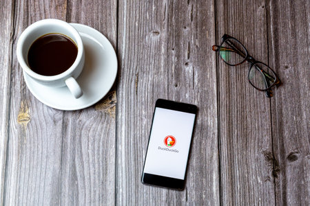 02/10/2021 Portsmouth, Hampshire, UK A mobile phone or cell phone laid on a wooden table with the DuckDuckGo app open on screen next to a coffeeのeditorial素材