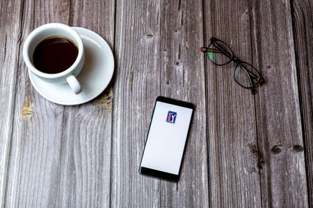 02/10/2021 Portsmouth, Hampshire, UK A mobile phone or cell phone laid on a wooden table with the PGA tour golf app open on screen next to a coffeeのeditorial素材