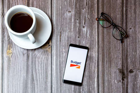 02/10/2021 Portsmouth, Hampshire, UK A mobile phone or cell phone laid on a wooden table with the Budget car rental app open on screenのeditorial素材
