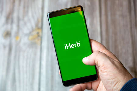 02-10-2021 Portsmouth, hampshire, UK A mobile phone or cell phone being held by a hand with the iHerb app open on screenのeditorial素材