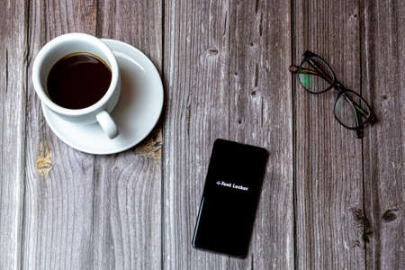 02/10/2021 Portsmouth, Hampshire, UK A mobile phone or cell phone laid on a wooden table with the Foot locker app open on screen next to a coffeeのeditorial素材