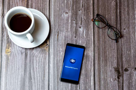02/10/2021 Portsmouth, Hampshire, UK A mobile phone or cell phone laid on a wooden table with the National Rail enquiries app open on screen next to a coffeeのeditorial素材