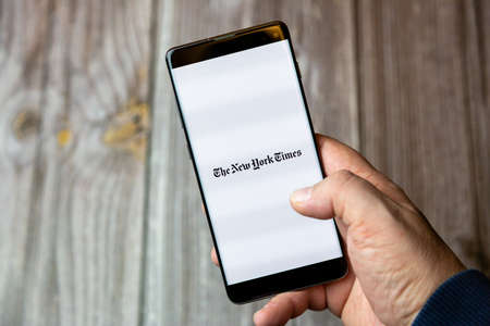 02-10-2021 Portsmouth, hampshire, UK A mobile phone or cell phone being held by a hand with the New York Times app open on screenのeditorial素材