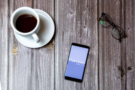 02/10/2021 Portsmouth, Hampshire, UK A mobile phone or cell phone laid on a wooden table with the Curvissa app open on screen next to a coffeeのeditorial素材