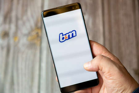 02-10-2021 Portsmouth, hampshire, UK A mobile phone or cell phone being held by a hand with the B&M app open on screenのeditorial素材