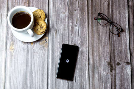 02-15-2021 Portsmouth, Hampshire, UK A mobile phone or cell phone laid on a wooden table with the XBOX app open on screenのeditorial素材
