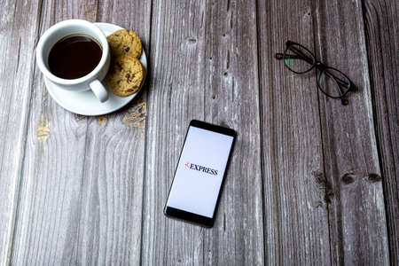 02-15-2021 Portsmouth, Hampshire, UK A mobile phone or cell phone laid on a wooden table with the express news app open on screenのeditorial素材