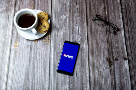 02-15-2021 Portsmouth, Hampshire, UK A mobile phone or cell phone laid on a wooden table with the Metro news app open on screenのeditorial素材
