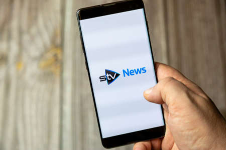 02-15-2021 Portsmouth, Hampshire, UK A mobile phone or cell phone being held in a hand with the STV news app open on screenのeditorial素材