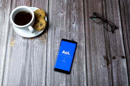 02-15-2021 Portsmouth, Hampshire, UK A mobile phone or cell phone laid on a wooden table with the AOL app open on screenのeditorial素材