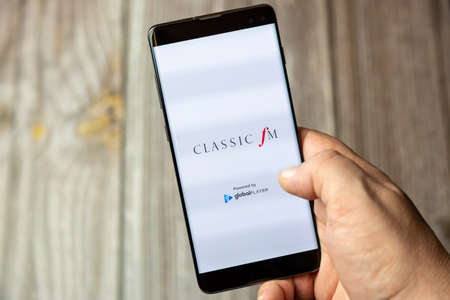 02-15-2021 Portsmouth, Hampshire, UK A mobile phone or cell phone being held in a hand with the Classic FM app open on screenのeditorial素材