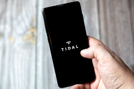 02-15-2021 Portsmouth, Hampshire, UK A mobile phone or cell phone being held in a hand with the Tidal app open on screenのeditorial素材