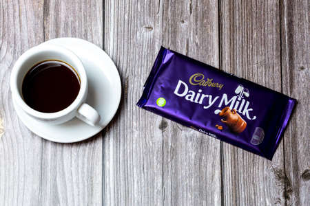 02-24-2021 Portsmouth, Hampshire, UK A Bar of Cadbury Dairy Milk chocolate lad on a wooden table next to a cup of coffeeのeditorial素材