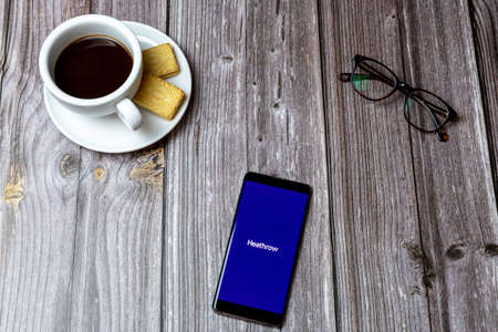02-24-2021 Portsmouth, Hampshire, UK A mobile phone or cell phone on a wooden table with the app Heathrow open next to a coffee and glassesのeditorial素材