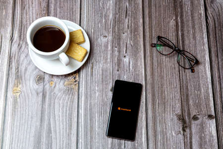 02-24-2021 Portsmouth, Hampshire, UK A mobile phone or cell phone on a wooden table with the Chrunchyroll app open next to a coffee and glassesのeditorial素材