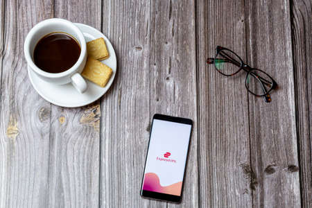 02-24-2021 Portsmouth, Hampshire, UK A mobile phone or cell phone on a wooden table with the Express VPN app open next to a coffee and glassesのeditorial素材