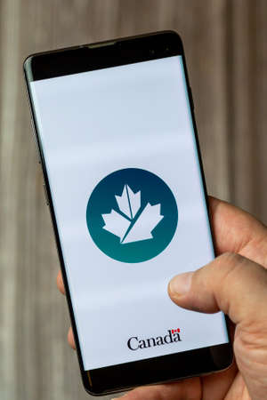 02-24-2021 Portsmouth, Hampshire, UK A mobile phone or cell phone being held by a hand with the Canada business app open on screenのeditorial素材