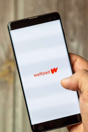 02-24-2021 Portsmouth, Hampshire, UK A mobile phone or cell phone being held by a hand with the Wattpad app open on screenのeditorial素材