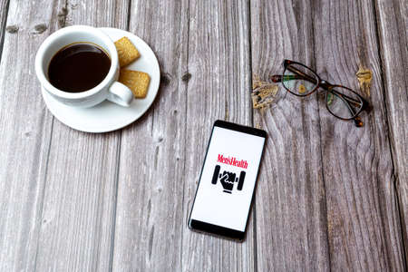 03-03-2021 Portsmouth, Hampshire, UK A mobile phone or cell phone laid on a wooden table with the Mens health personal trainer app open next to a coffeeのeditorial素材