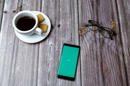 03-03-2021 Portsmouth, Hampshire, UK A mobile phone or cell phone laid on a wooden table with the Ufirst app open next to a coffeeのeditorial素材