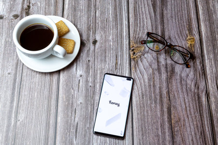 03-03-2021 Portsmouth, Hampshire, UK A mobile phone or cell phone laid on a wooden table with the Honey Shopping app open next to a coffeeのeditorial素材