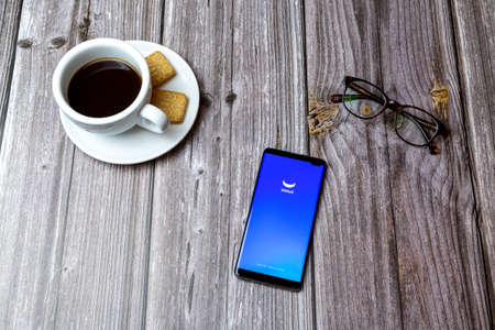 03-03-2021 Portsmouth, Hampshire, UK A mobile phone or cell phone laid on a wooden table with the Webull stocks app open next to a coffeeのeditorial素材
