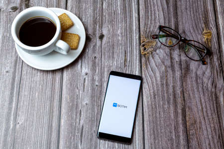 03-03-2021 Portsmouth, Hampshire, UK A mobile phone or cell phone laid on a wooden table with the Botim app open next to a coffeeのeditorial素材