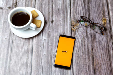 03-03-2021 Portsmouth, Hampshire, UK A mobile phone or cell phone laid on a wooden table with the Ziffit app open next to a coffeeのeditorial素材