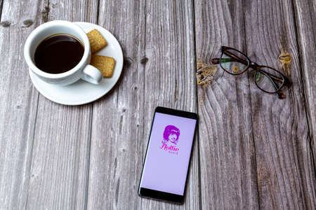 03-03-2021 Portsmouth, Hampshire, UK A mobile phone or cell phone laid on a wooden table with the Hollie Guard app open next to a coffeeのeditorial素材