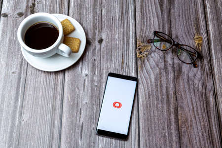 03-03-2021 Portsmouth, Hampshire, UK A mobile phone or cell phone laid on a wooden table with the MyHeritage app open next to a coffeeのeditorial素材