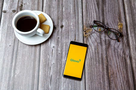 03-03-2021 Portsmouth, Hampshire, UK A mobile phone or cell phone laid on a wooden table with the Glovo app open next to a coffeeのeditorial素材