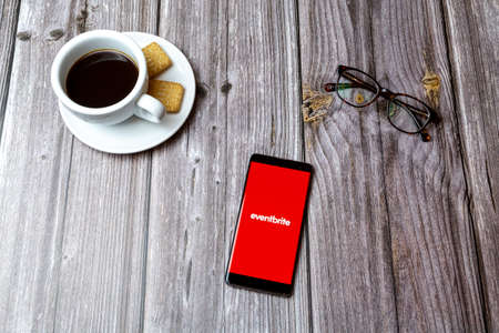 03-03-2021 Portsmouth, Hampshire, UK A mobile phone or cell phone laid on a wooden table with the Eventbrite app open next to a coffeeのeditorial素材