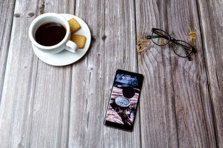 03-03-2021 Portsmouth, Hampshire, UK A mobile phone or cell phone laid on a wooden table with the travel magazine app open next to a coffeeのeditorial素材