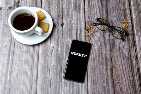 03-03-2021 Portsmouth, Hampshire, UK A mobile phone or cell phone laid on a wooden table with the scruff Gay Chat app open next to a coffeeのeditorial素材